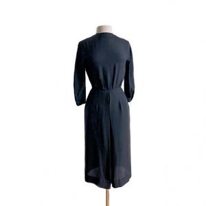 May include: A black midi dress with a simple, elegant design. The dress has a round neckline and three-quarter sleeves. The skirt is slightly flared and falls to just above the knee.