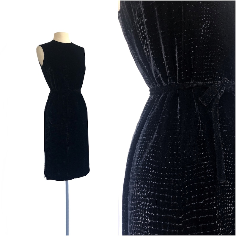 May include: A black sleeveless dress with a textured velvet fabric. The dress has a fitted bodice and a slightly flared skirt. It features a self-tie belt at the waist.