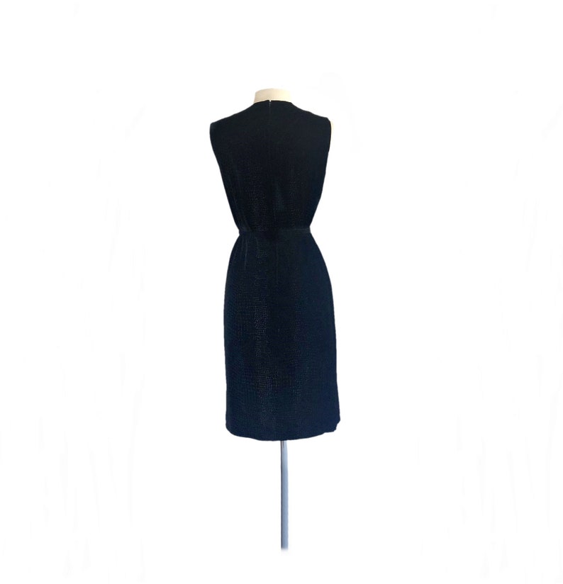 May include: A sleeveless black dress with a textured fabric. The dress has a fitted bodice and a slightly flared skirt.