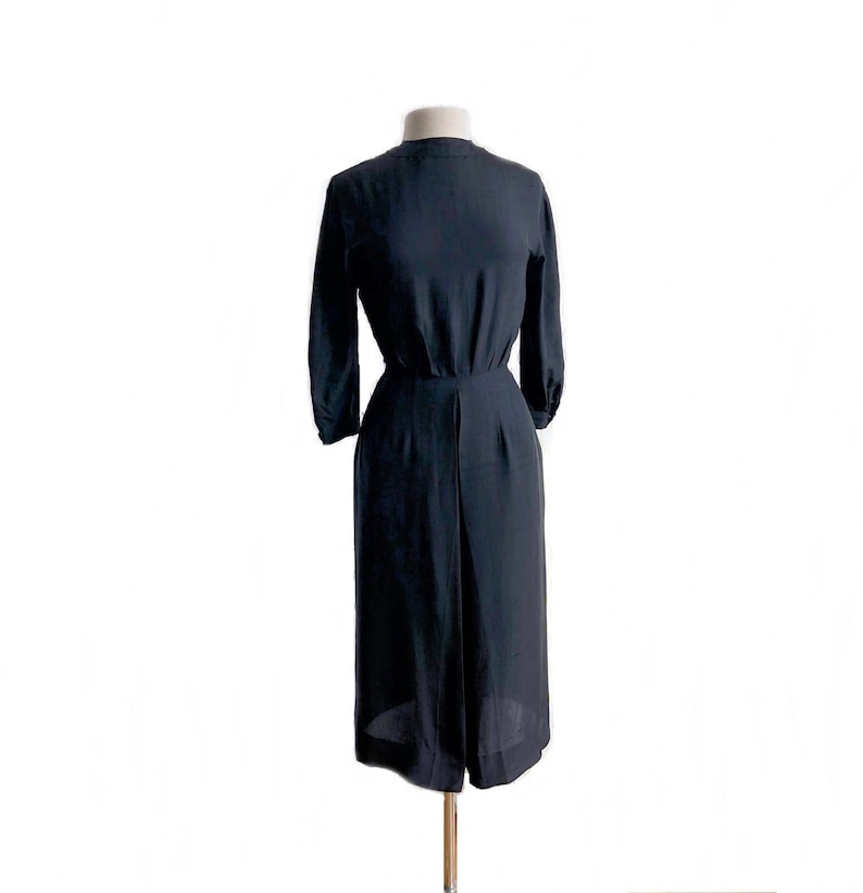 May include: A black midi dress with a simple, elegant design. The dress has a round neckline and three-quarter sleeves. The skirt is slightly flared and falls to just above the knee.
