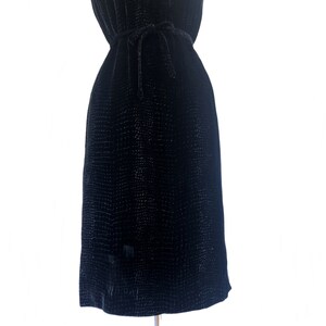 May include: A black velvet dress with a subtle textured pattern. The dress has a tie at the waist.