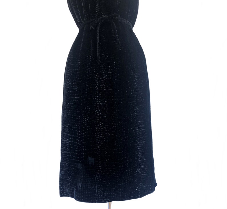 May include: A black velvet dress with a subtle textured pattern. The dress has a tie at the waist.