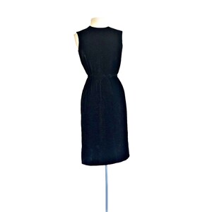 May include: A sleeveless black dress with a fitted bodice and a straight skirt. The dress is made of a textured fabric and has a simple, elegant design.
