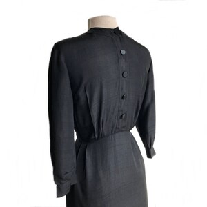 May include: A black long-sleeved dress with a button-up back. The dress has a fitted bodice and a slightly flared skirt.