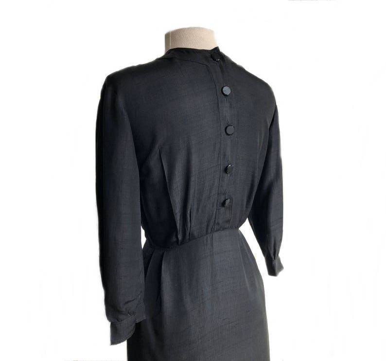 May include: A black long-sleeved dress with a button-up back. The dress has a fitted bodice and a slightly flared skirt.