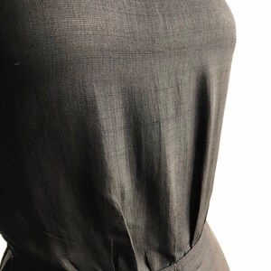 May include: A close-up of a black sleeveless dress with a gathered waistline. The fabric has a subtle texture.