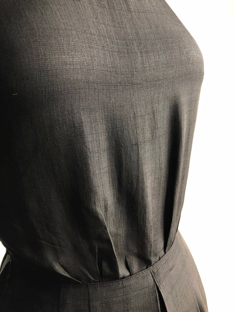 May include: A close-up of a black sleeveless dress with a gathered waistline. The fabric has a subtle texture.