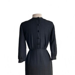 May include: A black long-sleeved dress with a button-up front and a fitted waist. The dress is made of a smooth, silky fabric.
