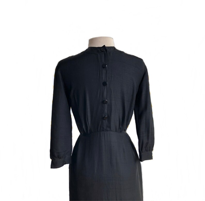 May include: A black long-sleeved dress with a button-up front and a fitted waist. The dress is made of a smooth, silky fabric.