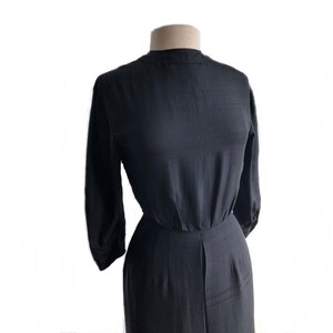 May include: A black, long-sleeved dress with a high neckline and a fitted bodice. The dress has a gathered waist and a flowing skirt.