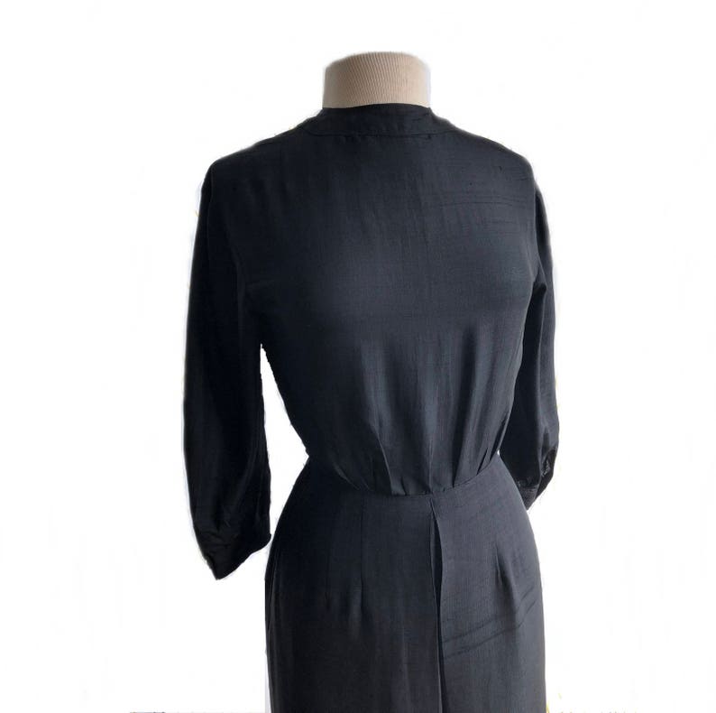 May include: A black, long-sleeved dress with a high neckline and a fitted bodice. The dress has a gathered waist and a flowing skirt.