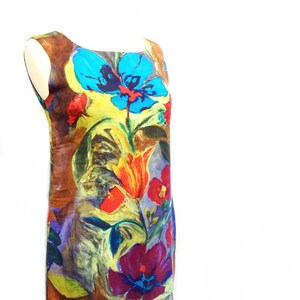 May include: A sleeveless dress with a colorful floral print. The dress features a variety of flowers in shades of blue, red, yellow, and purple. The background of the dress is a brown color.