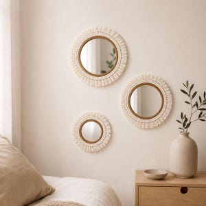 May include: Three circular wall mirrors featuring frames wrapped in natural tan rope and finished with a decorative fringe of off-white macrame cord. The mirrors vary in size and are arranged in a cluster on a plain, light-colored wall surface.