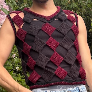 May include: A sleeveless crochet vest featuring a diamond-patterned lattice design in alternating solid black and shimmering dark red yarn. The vest has a round neckline and is worn over a plain black tank top, showcasing a textured, open-work construction.
