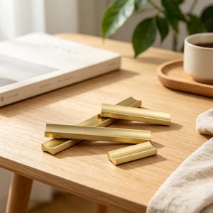 May include: A collection of three gold-colored metal cabinet pulls with a smooth, matte finish. The hardware features a concave, curved profile and a rectangular base, arranged in a cluster on a flat surface to display the metallic texture.
