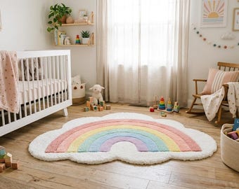 May include: A cloud-shaped area rug featuring a central rainbow design with pastel stripes in pink, yellow, green, blue, and purple, set against a white textured background. The rug is positioned on a wooden floor in a nursery room setting.