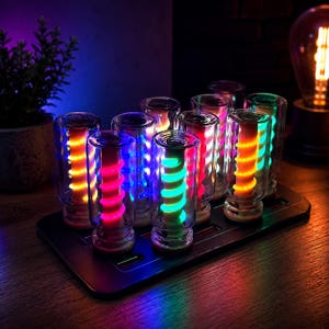 May include: A set of ten clear glass cylindrical containers arranged on a black rectangular base. Each container holds a central vertical rod with a glowing spiral light in various colours including orange, pink, blue, green, and yellow.