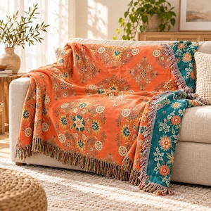 Könnte beinhalten: Eine gewebte Wohndecke mit einer leuchtend orangefarbenen Basis und einem sich wiederholenden Blumen- und geometrischen Muster in Blaugrün, Gelb und Creme. Die Decke hat einen dunkelblauen Rand und dekorative Fransen an den Kanten.