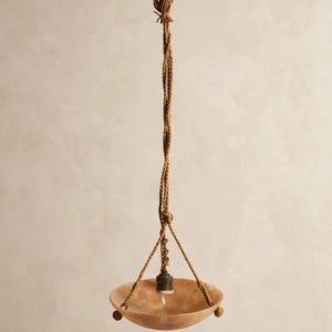 Może przedstawiać: Wisząca lampa wisząca z płytką, półprzezroczystą misą z kamienia w odcieniach bursztynu. Misa jest zawieszona na trzech skręconych brązowych sznurach, które łączą się w centralnym węźle, z pojedynczą oprawką żarówki umieszczoną wewnątrz misy.