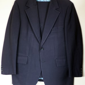 May include: A dark blue blazer with a single button closure and a patterned lining. The blazer has a classic fit and features two flap pockets on the front.