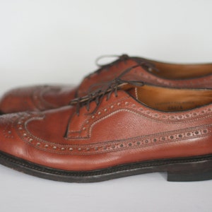 May include: A pair of brown leather brogue shoes with a lace-up closure. The shoes have a wingtip design and a decorative pattern of small holes.
