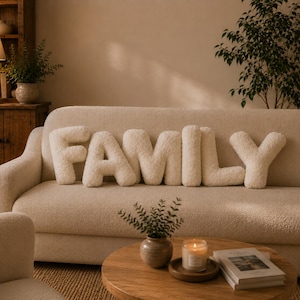 Peut inclure: Un ensemble de six coussins en forme de lettres de couleur crème, texturés et moelleux, disposés sur un canapé pour épeler le mot FAMILY. Chaque lettre est fabriquée dans un tissu doux et duveteux avec un aspect arrondi et rembourré.
