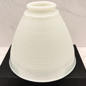 May include: A white milk glass lamp shade featuring a bell-shaped silhouette and a textured grid pattern across its surface. The shade has a smooth, circular opening at the top and a wider, open base, designed for light diffusion in a fixture.