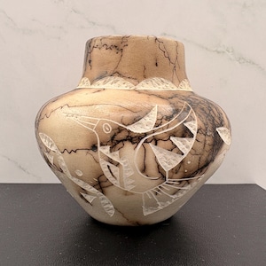May include: A tan and cream-colored ceramic vase with a rounded body and a narrow neck. The surface features dark, thin, web-like crackle patterns and white etched designs of a bird in flight, surrounded by leaf-like shapes.