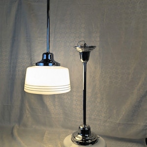 May include: Two pendant lights with polished chrome stems and circular ceiling mounts. Each fixture features a white glass shade with three horizontal black lines around the base. One light is illuminated, while the other is unlit.