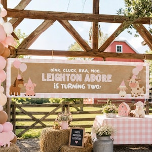 Puede incluir: Una pancarta rectangular con fondo color canela y bordes de cuadros rosas, con el texto OINK, CLUCK, BAA, MOO... LEIGHTON ADORE IS TURNING TWO! e ilustraciones de un caballo, un cerdo, una oveja y una vaca con gorros de fiesta.