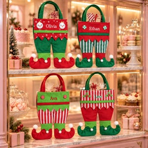 May include: Four fabric gift bags shaped like elf trousers with handles. Each bag features a personalised name: Olivia, Ethan, Ava, or Leo. The designs include red and green colour schemes, white pom-poms on the curled toes, and striped patterns.