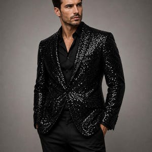 Può includere: Un blazer nero con paillettes caratterizzato da un bavero a lancia, maniche lunghe e due tasche frontali con patta. Il blazer è indossato sopra una camicia nera abbottonata e abbinato a pantaloni neri, creando un completo monocromatico riflettente.