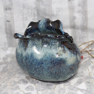 May include: A small, blue and white ceramic vase with a unique, organic shape. The vase has a speckled glaze and a slightly textured surface.