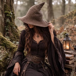 May include: A brown crocheted pointed hat with a wide brim worn with a black long-sleeved dress featuring lace-up front detailing, intricate embroidery on the sleeves, and a wide brown leather belt with a circular buckle and hanging metal charms.