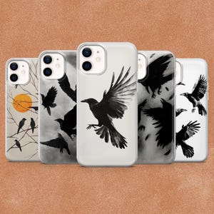 May include: Five clear smartphone cases arranged in a row, each featuring black and white illustrations of crows. Designs include crows perched on bare branches with an orange sun, crows in flight against a cloudy sky, and single flying crows.