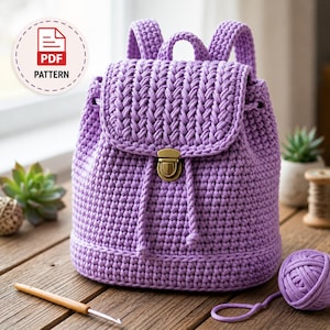 May include: A lavender crochet backpack featuring a textured stitch pattern, a top flap with a metallic gold-tone push-lock closure, and two shoulder straps. A circular badge in the upper left corner displays the text PDF PATTERN.