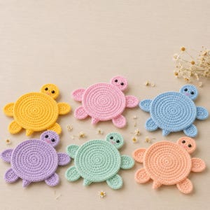 Puede incluir: Seis posavasos de ganchillo con forma de tortuga en amarillo, rosa, azul claro, morado, verde menta y melocotón. Cada posavasos presenta un patrón de caparazón circular, cuatro aletas pequeñas y una cabeza con dos ojos de cuentas negras.