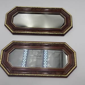May include: Two octagonal wall mirrors featuring dark brown wood frames with a burl wood grain pattern. Each mirror is accented by a thin, textured gold-colored metal trim along the inner and outer edges of the frame, surrounding the glass.