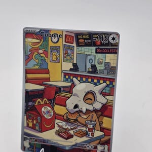 Puede incluir: Una tarjeta coleccionable rectangular que muestra a un personaje Cubone sentado en un restaurante de comida rápida. La tarjeta presenta una caja de Happy Meal, papas fritas y una bebida en la mesa. El fondo muestra un menú con Big Mac y 115 HP.