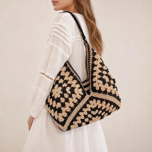 May include: A crochet shoulder bag featuring a geometric granny square pattern in alternating black and beige yarn. The bag has a wide, integrated strap and a soft, slouchy construction, showcasing a repeating square motif throughout the design.