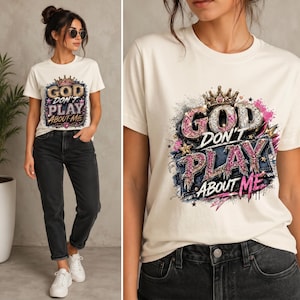 May include: A cream-colored short-sleeve t-shirt featuring a graphic print with the text "GOD DON'T PLAY ABOUT ME" in a glittery, multi-colored font. The design includes a crown, stars, and denim-textured elements with pink and blue accents.