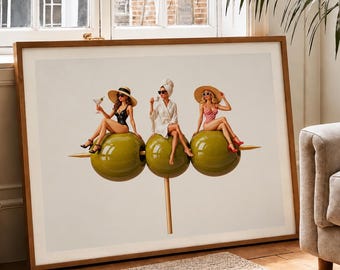 May include: A framed art print featuring three figures sitting on large green olives skewered on a toothpick. The left figure wears a black swimsuit and sun hat, the center wears a white robe and towel, and the right wears a red patterned swimsuit.