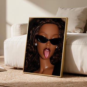 May include: A framed vertical wall art print featuring a close-up portrait of a doll with dark brown skin, long wavy dark brown hair, and black cat-eye sunglasses. The doll has dark red lipstick, a visible tongue, and small square stud earrings.