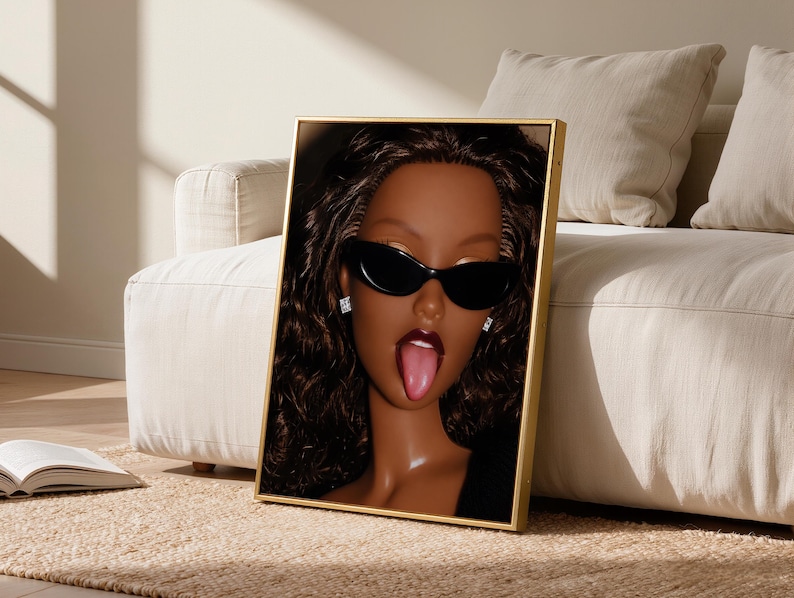 May include: A framed vertical wall art print featuring a close-up portrait of a doll with dark brown skin, long wavy dark brown hair, and black cat-eye sunglasses. The doll has dark red lipstick, a visible tongue, and small square stud earrings.