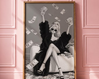 May include: A framed wall art print featuring a doll with blonde hair wearing black sunglasses and a black faux fur coat, sitting in a white armchair. The doll holds US dollar bills while more bills fall through the air around the chair.