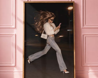 May include: A framed wall art print featuring a doll with long brown hair, wearing a white fuzzy jacket, a white top, and light blue flared jeans with a chain belt. The doll is holding a pink smartphone, wearing sunglasses, and white high heels.