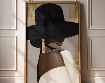 May include: A framed wall art print depicting a person wearing a wide-brimmed black hat and a white off-the-shoulder top. The figure has dark skin and wears a long, rectangular gold earring. The background features abstract gold leaf accents.