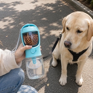 Puede incluir: Un dispensador portátil de agua y comida para mascotas de color azul claro, con un depósito inferior transparente para agua y un compartimento superior lleno de pienso marrón, equipado con un botón circular y una correa gris.