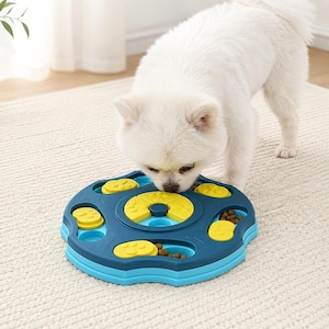 Puede incluir: Un juguete rompecabezas circular para mascotas en azul oscuro y azul claro, con compartimentos deslizantes amarillos con texturas de huellas. El juguete contiene trozos de comida marrón en sus pistas para la alimentación interactiva.