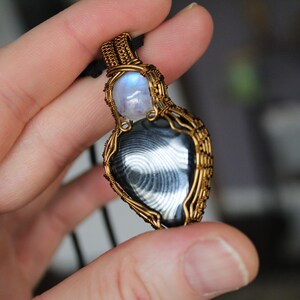 May include: A gold wire wrapped pendant featuring a black and white banded agate stone and a round moonstone.